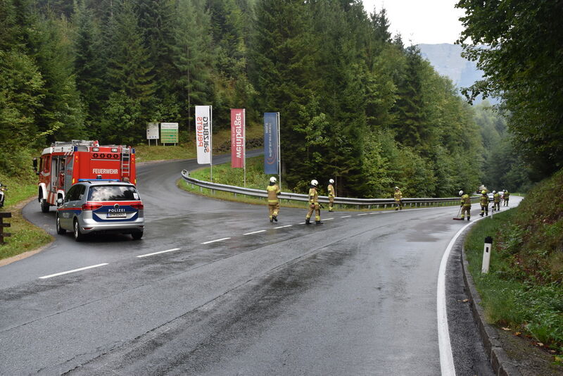 Feuerwehr und Polizei im Einsatz auf nasser Straße in Bergregion, Österreich.