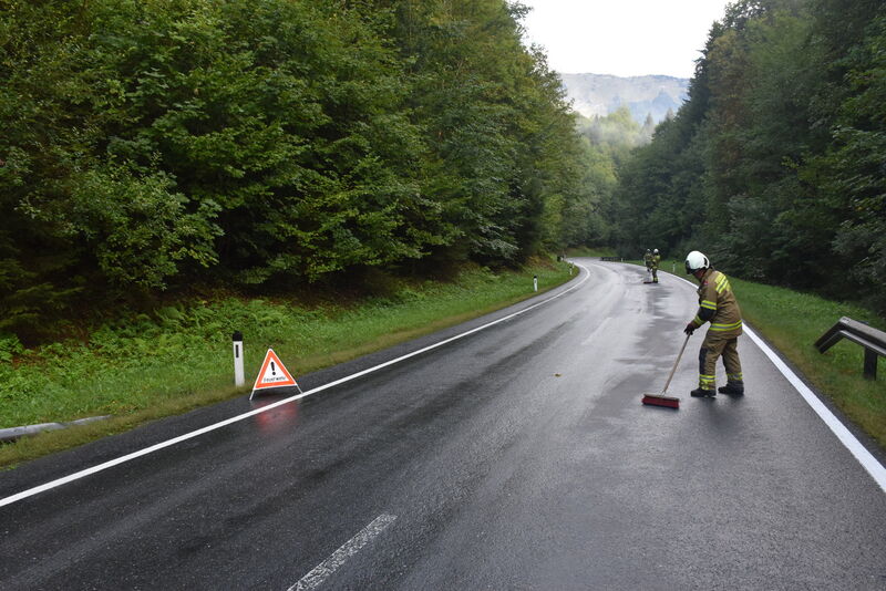 Feuerwehrkräfte reinigen nasse Straße mit Besen, Warnschild auf der Fahrbahn